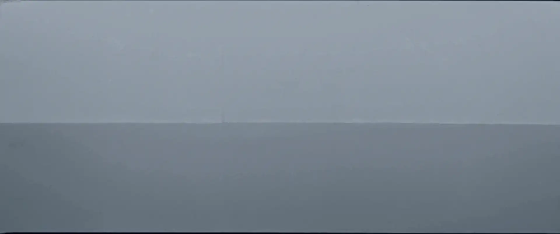 Flat grey water meeting a grey sky at a calm, open horizon